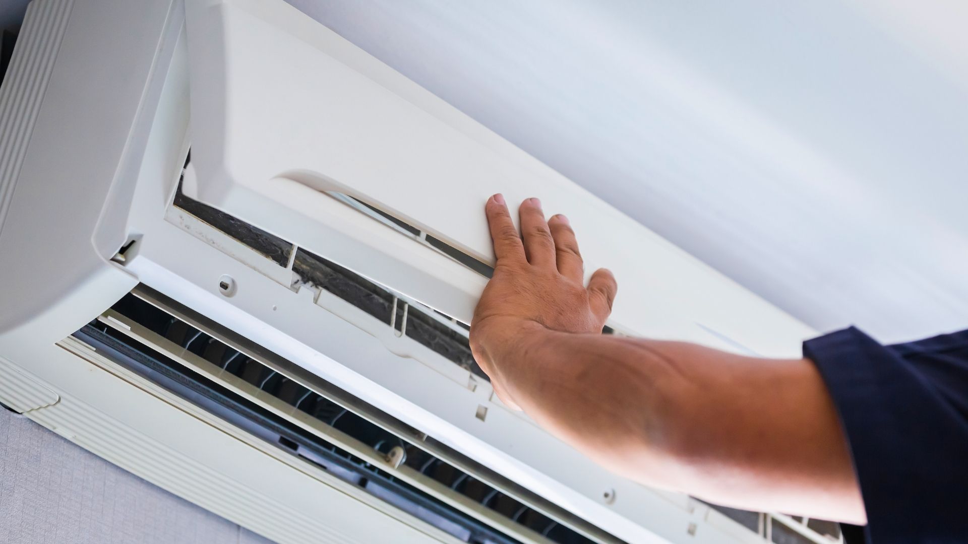 Hand opening a white wall-mounted air conditioner vent for cleaning or adjustment