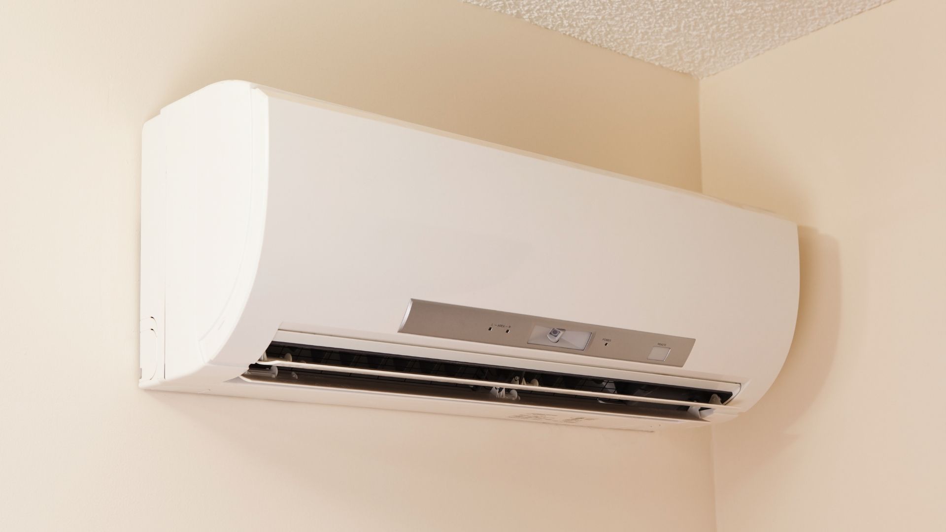 White wall-mounted air conditioner on a beige wall near the ceiling