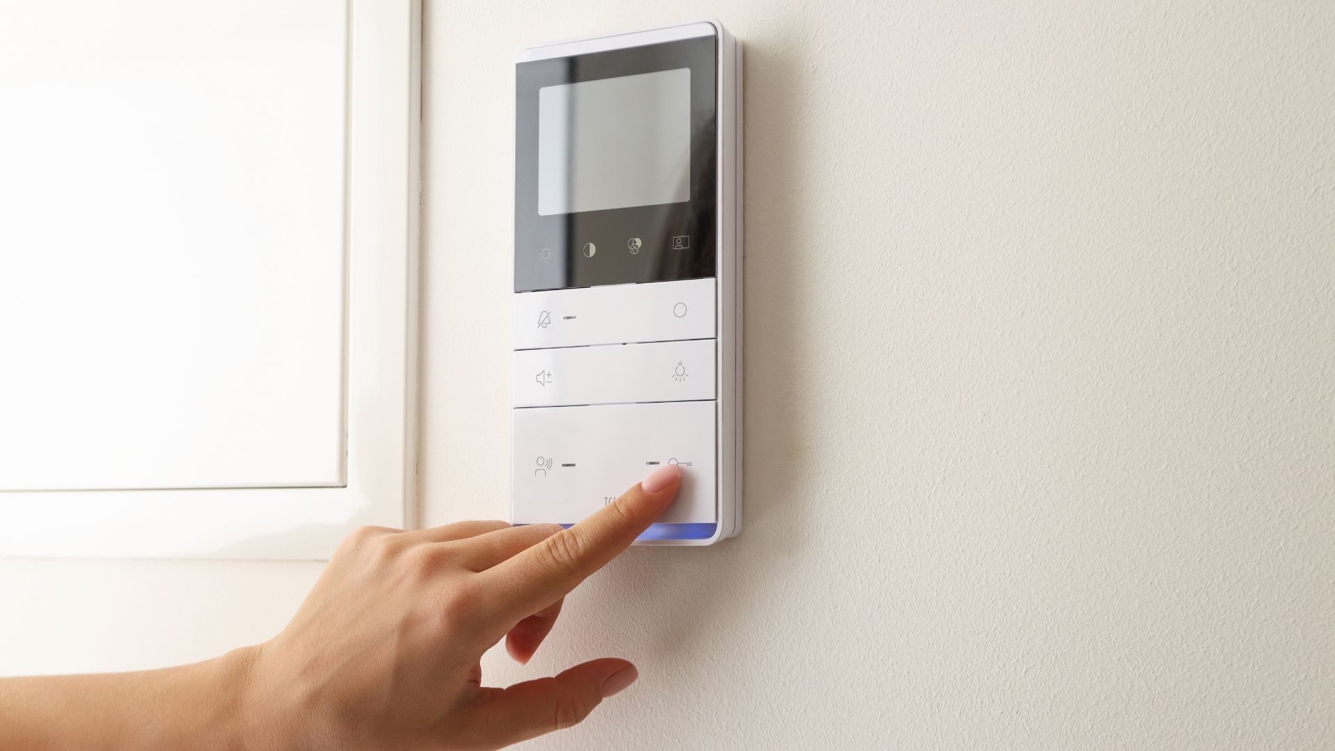 Hand pressing a wall-mounted video intercom with a small screen and buttons