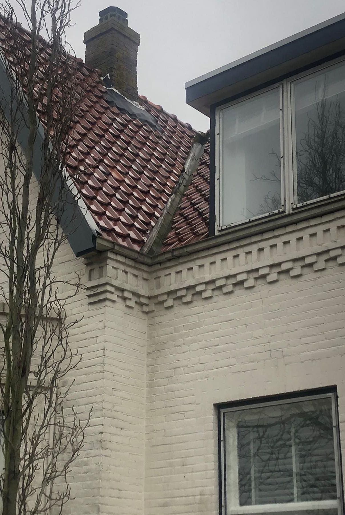 een wit bakstenen gebouw met een rood pannendak en een raam.