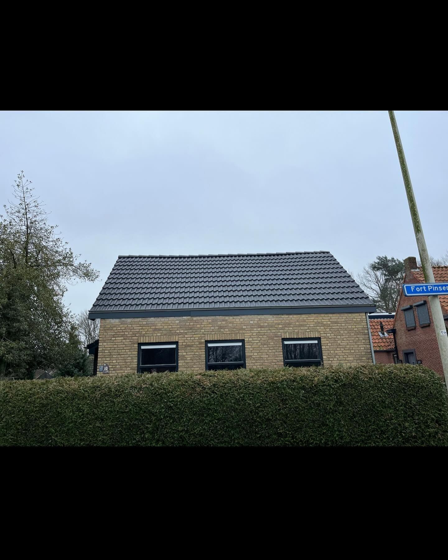 een huis met een zwart dak en een heg ervoor.