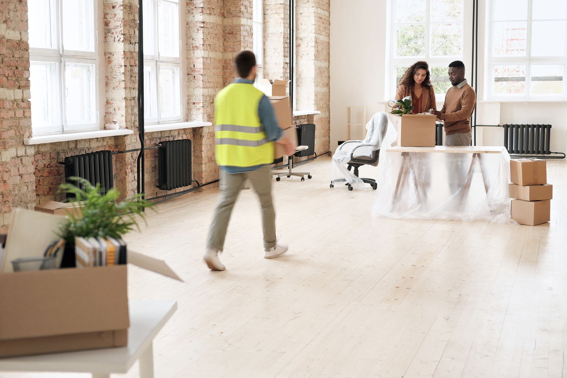 A man in a yellow vest is carrying boxes in an office.