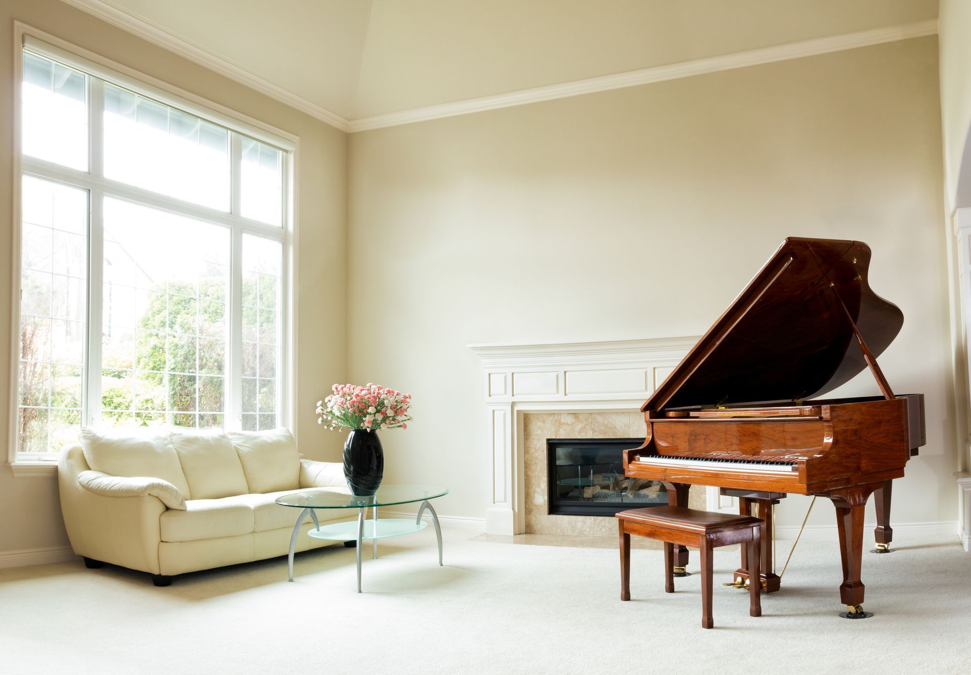 Living room with grand piano, sofa, large window, fireplace, and flowers.
