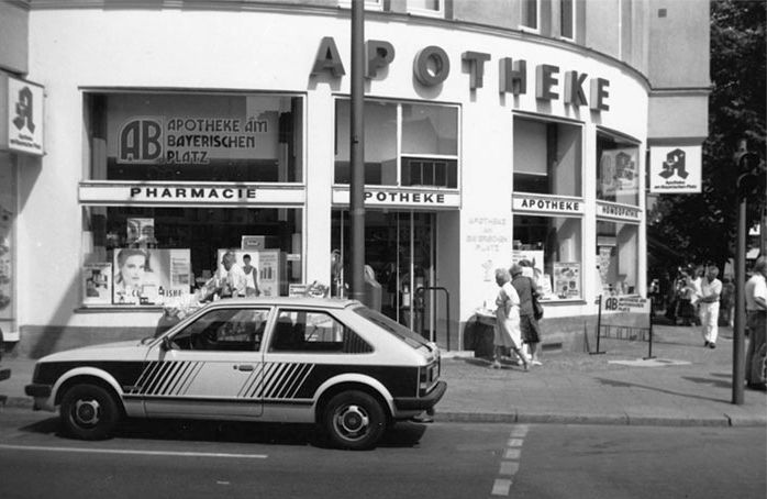 Ein Schwarzweißfoto einer Apotheke mit einem davor geparkten Auto
