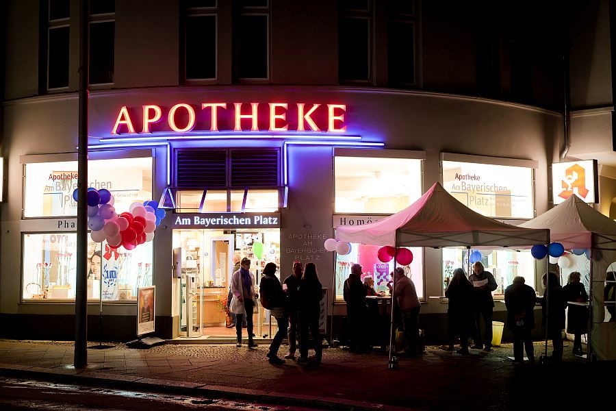 Eine Gruppe von Menschen steht nachts vor einer Apotheke.