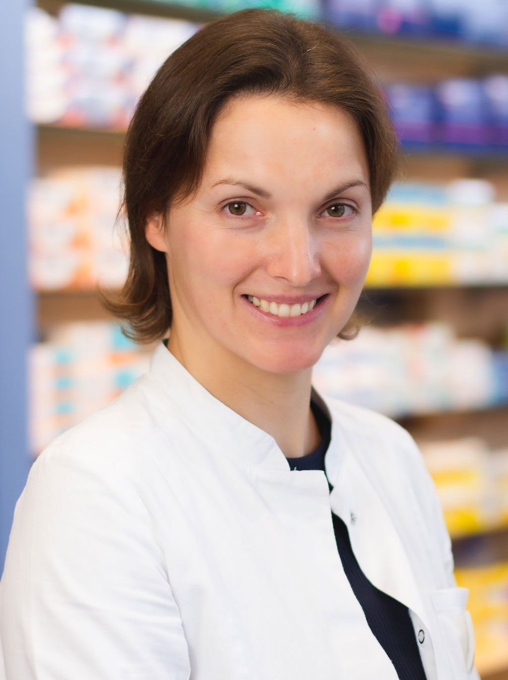 Eine Frau im weißen Kittel lächelt in einer Apotheke