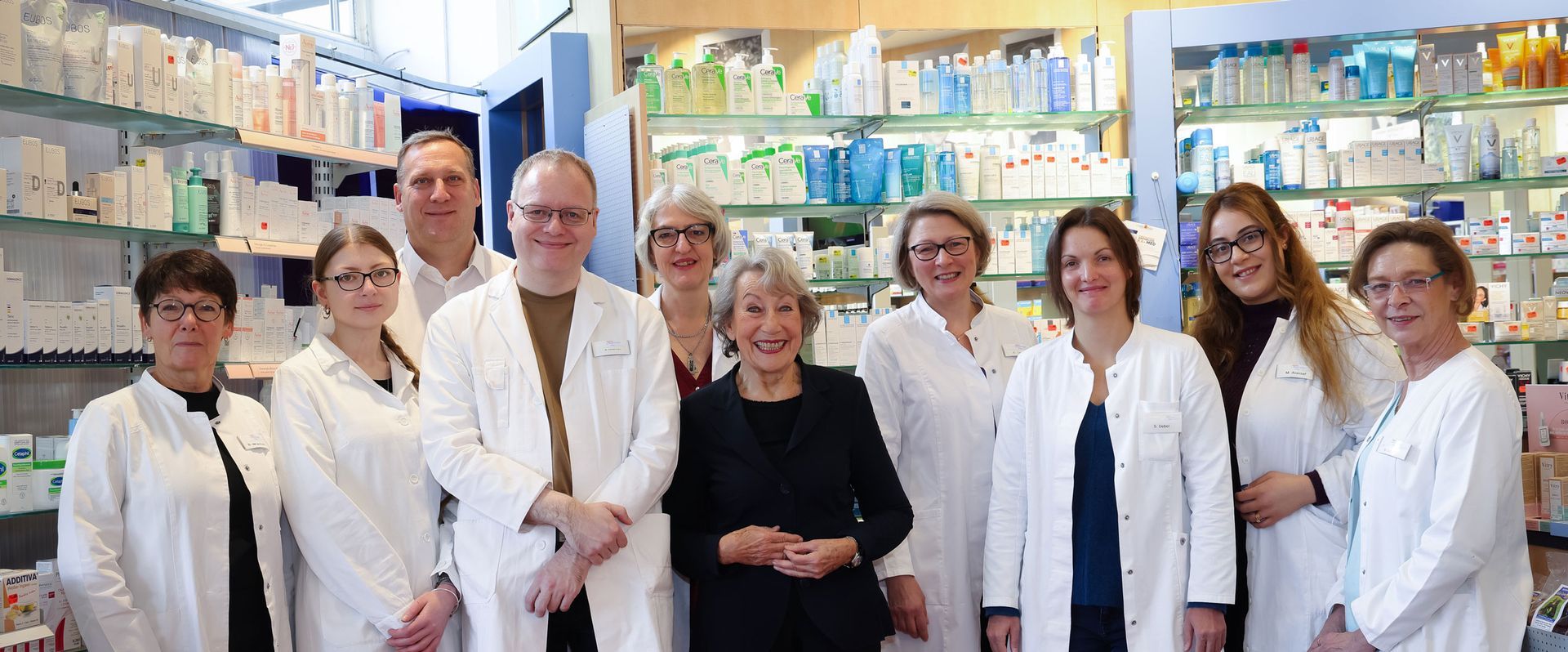 Eine Gruppe von Menschen in weißen Kitteln posiert in einer Apotheke für ein Foto.
