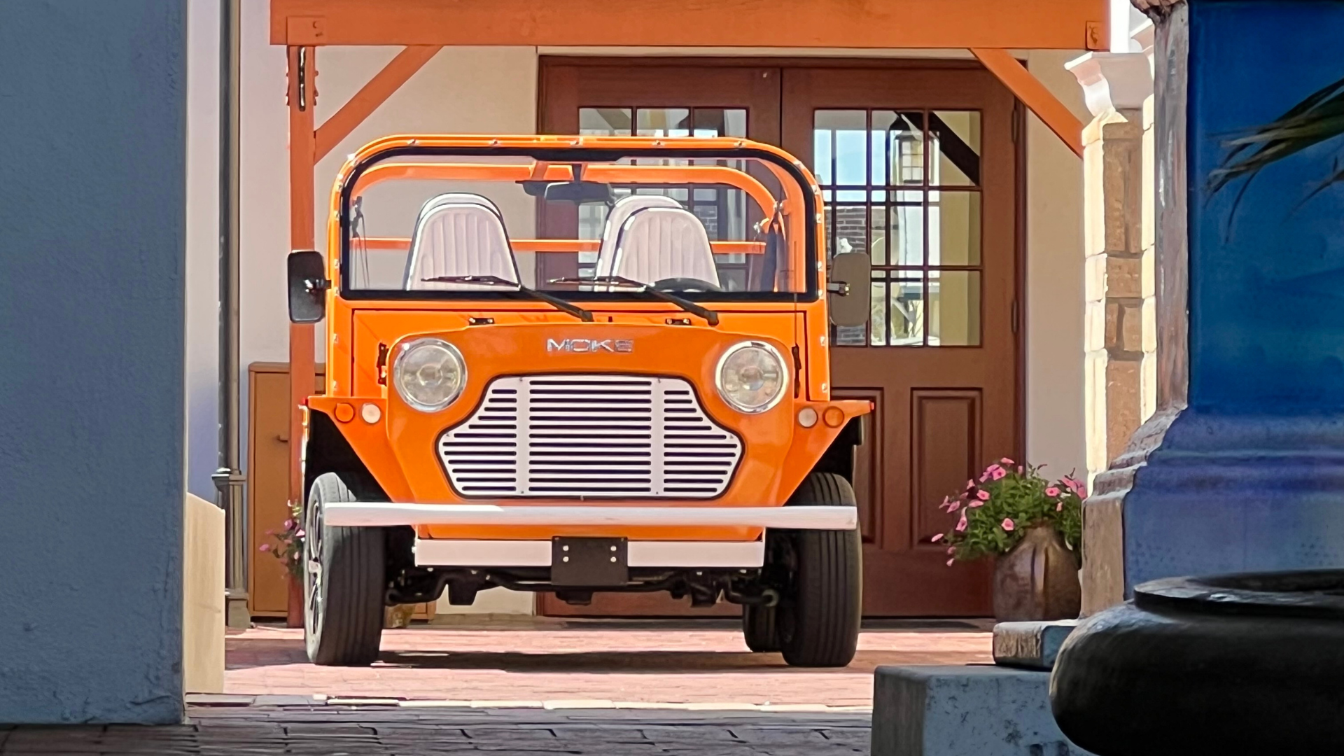 Orange electric vehicle parked in front of a building with a wooden door.