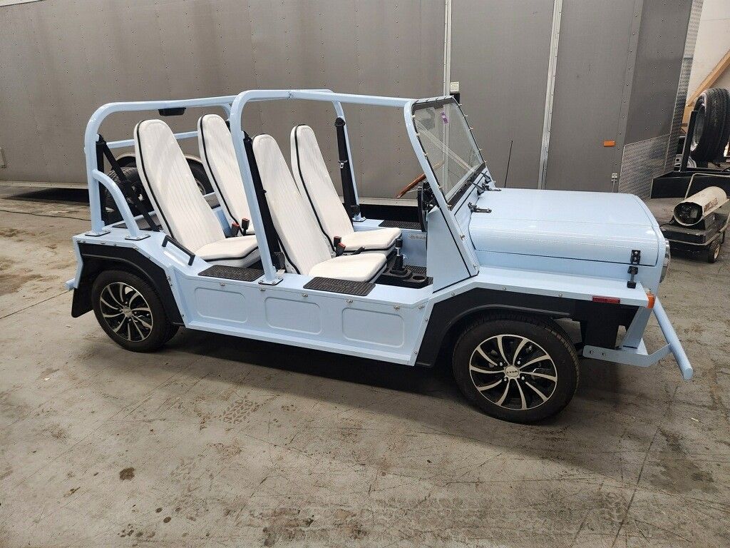 Light blue open-top electric vehicle with white seats, black wheels, in a garage setting.