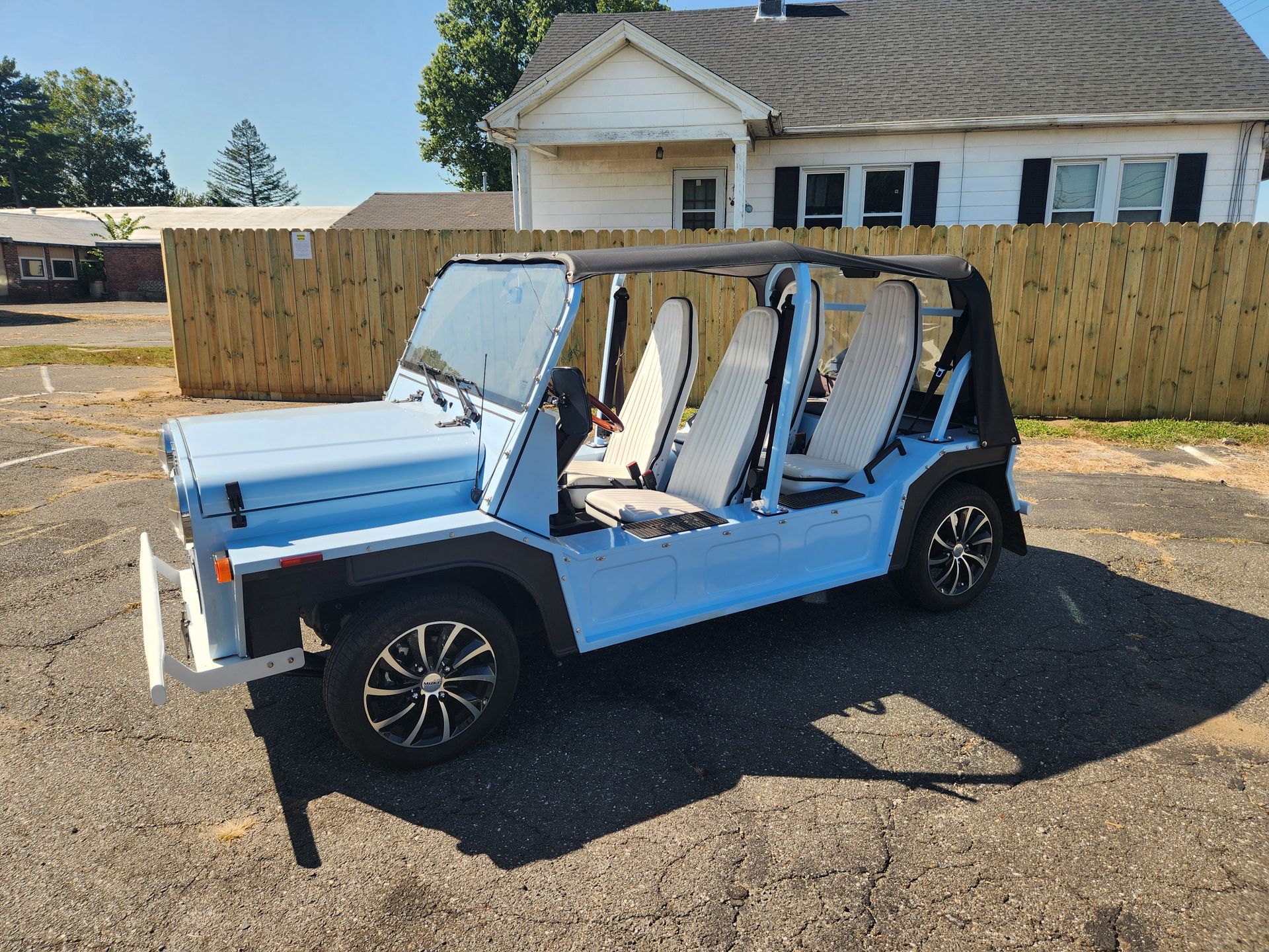 Light blue open-top car parked outside, with a wooden fence and building in the background.