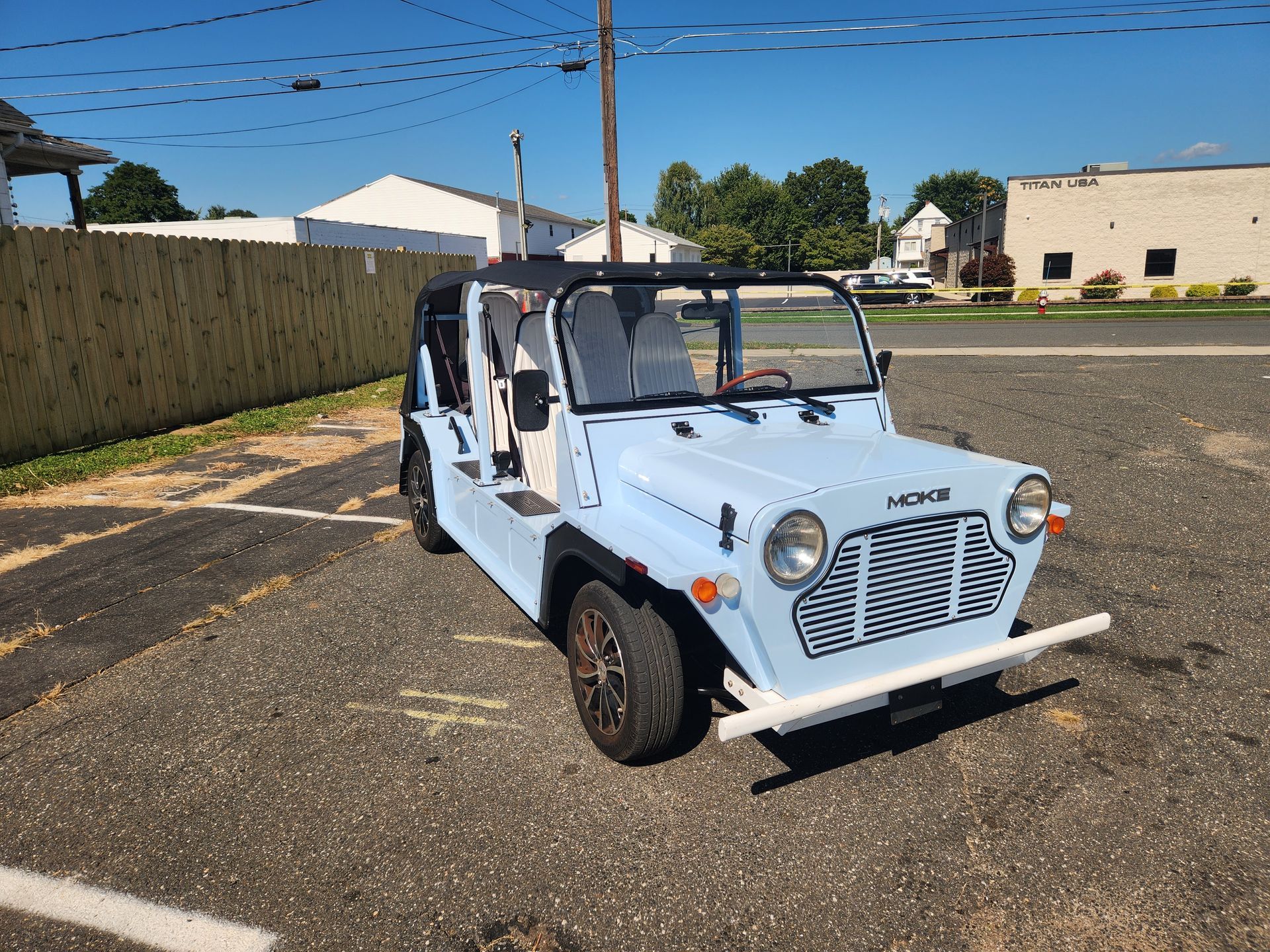 Light blue open-top car parked outside, with a wooden fence and building in the background.