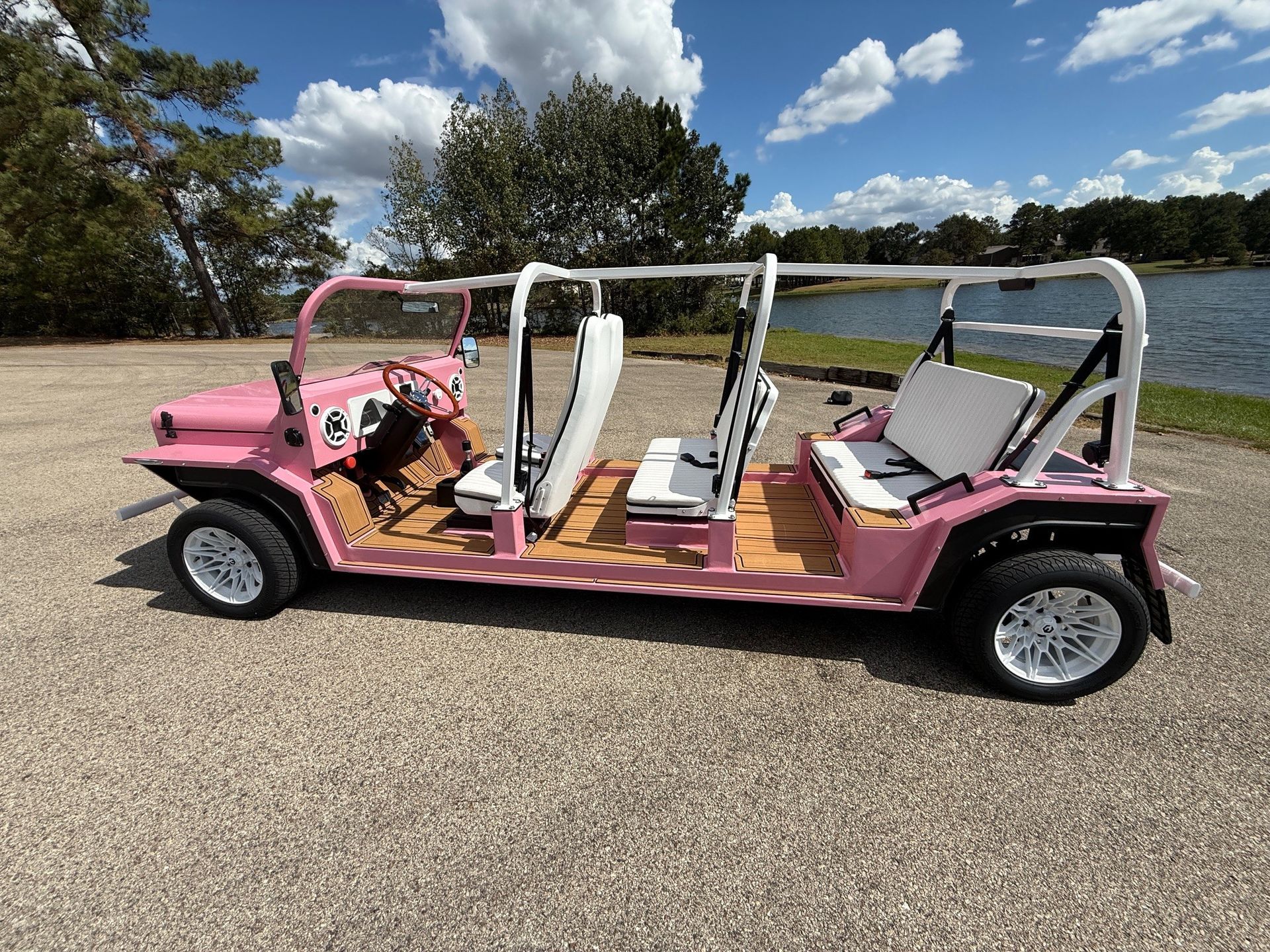 Pink and white golf cart with a wooden floor, parked outside on a sunny day.