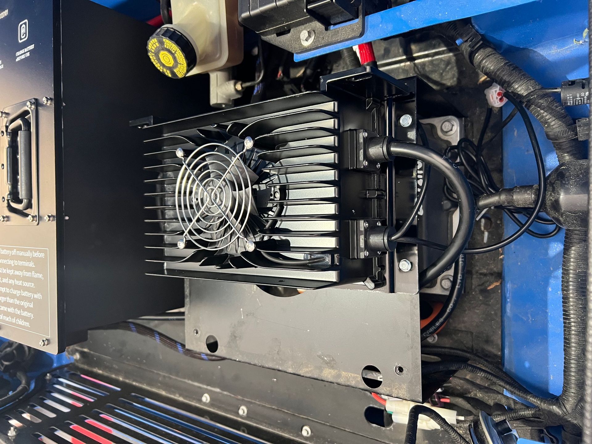 Black electronic component with a fan, mounted in a blue vehicle. Wires and other components are visible.