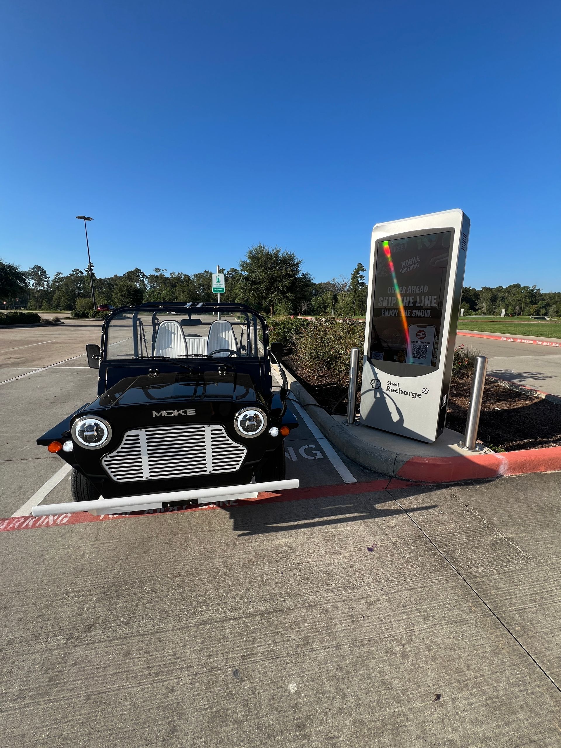 Black electric vehicle parked next to a charging station on a sunny day.