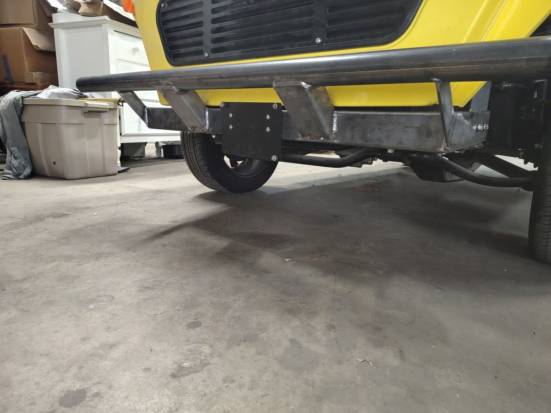 Yellow vehicle's rear end with a black metal bumper, and a black license plate mount over a tire.