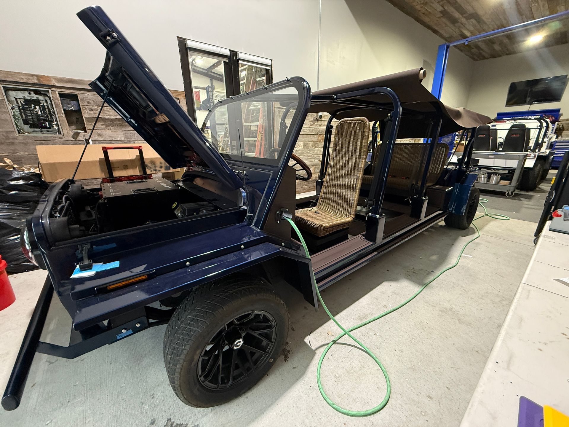 Black open-air six-seat moke golf cart parked on a paved drive in a sunny, tree-lined area