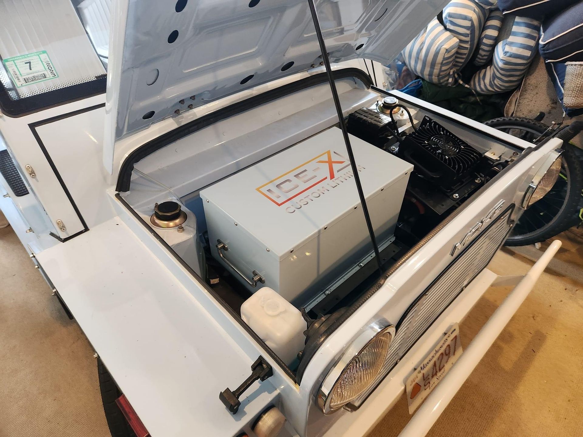 White vehicle's open hood revealing a large white box with red labeling, presumably the engine.