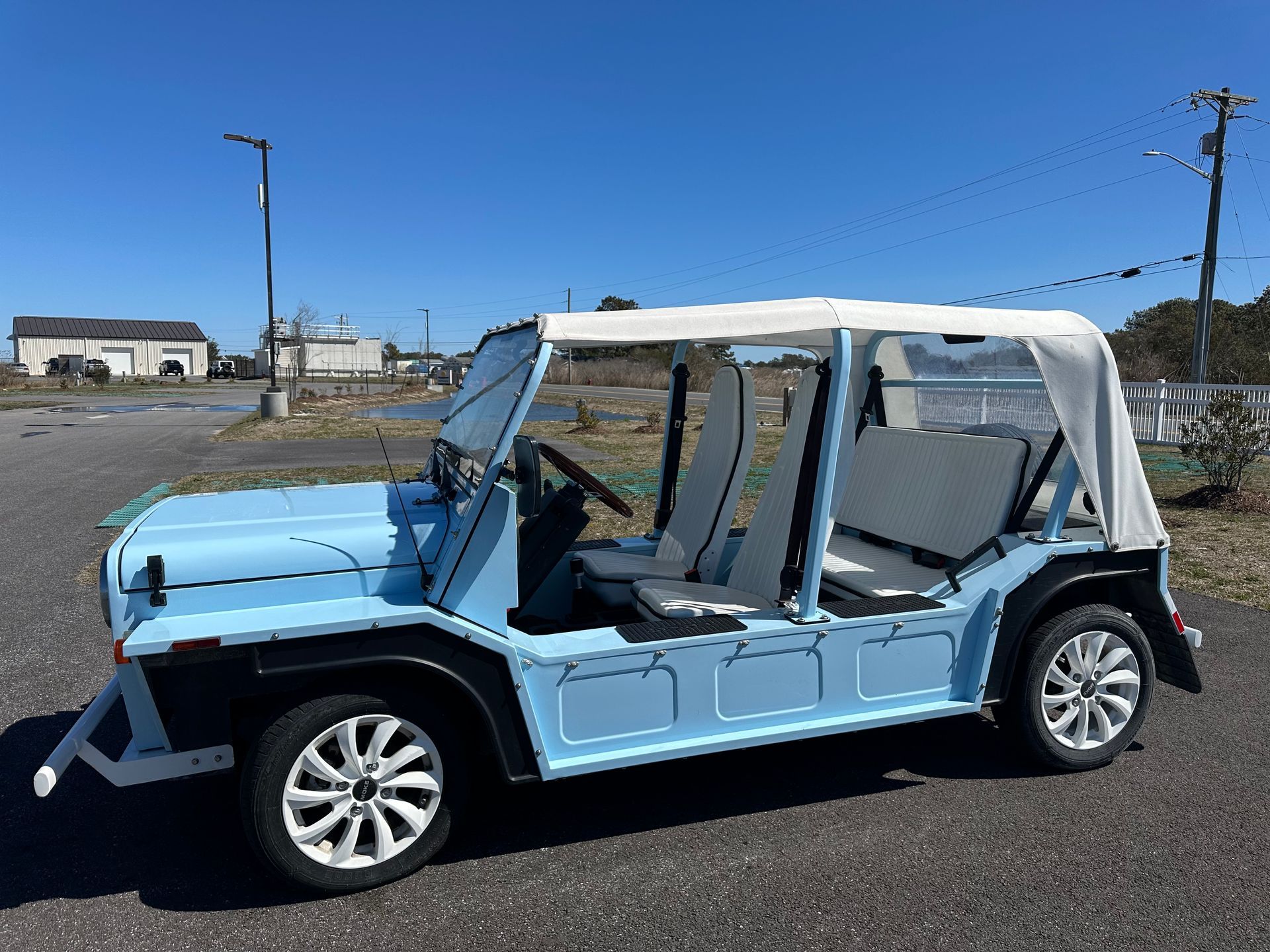 Light blue Moke car with a white top, parked on asphalt.