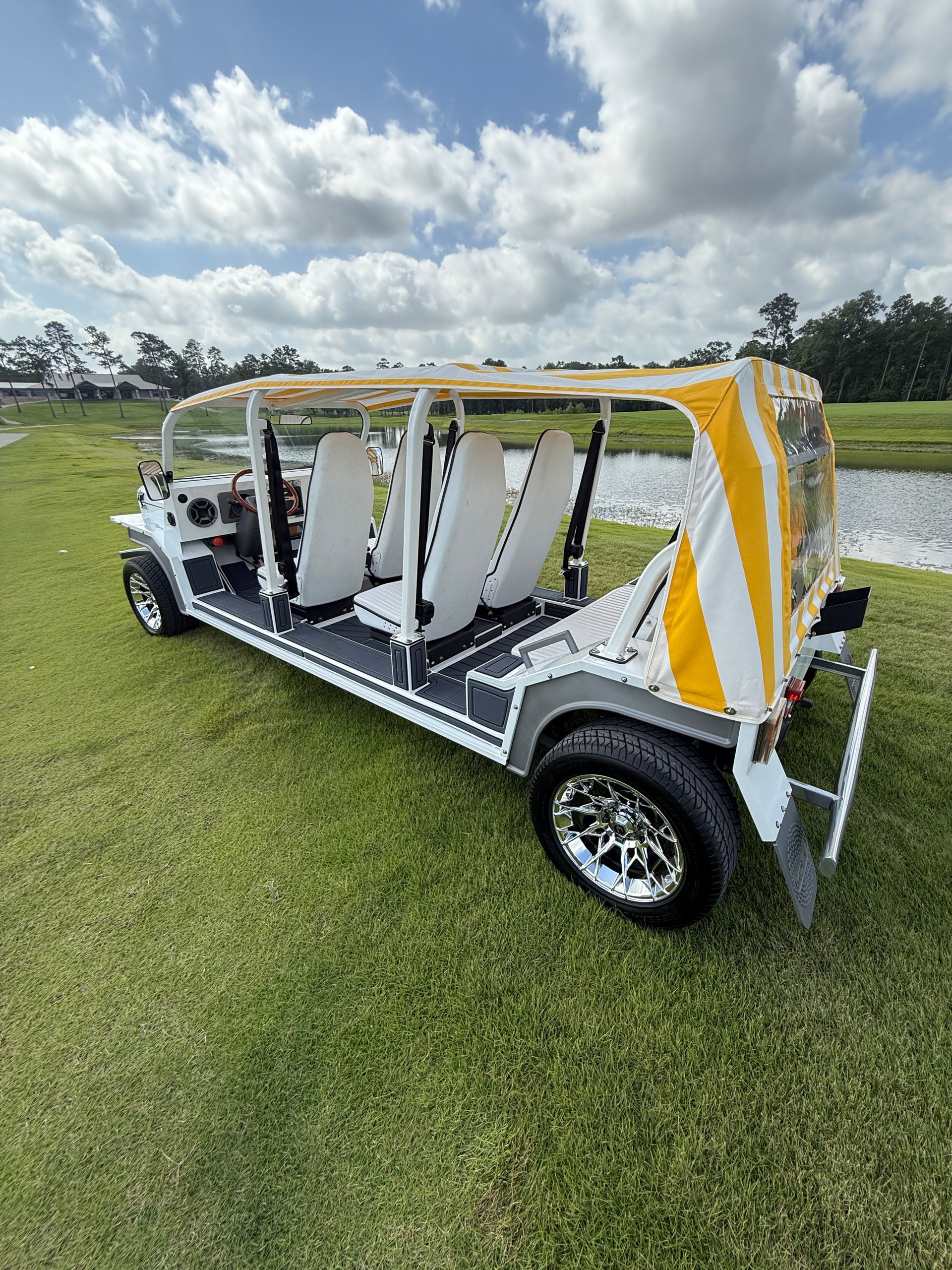 White multi-passenger golf cart on green grass near a pond, under a cloudy sky.