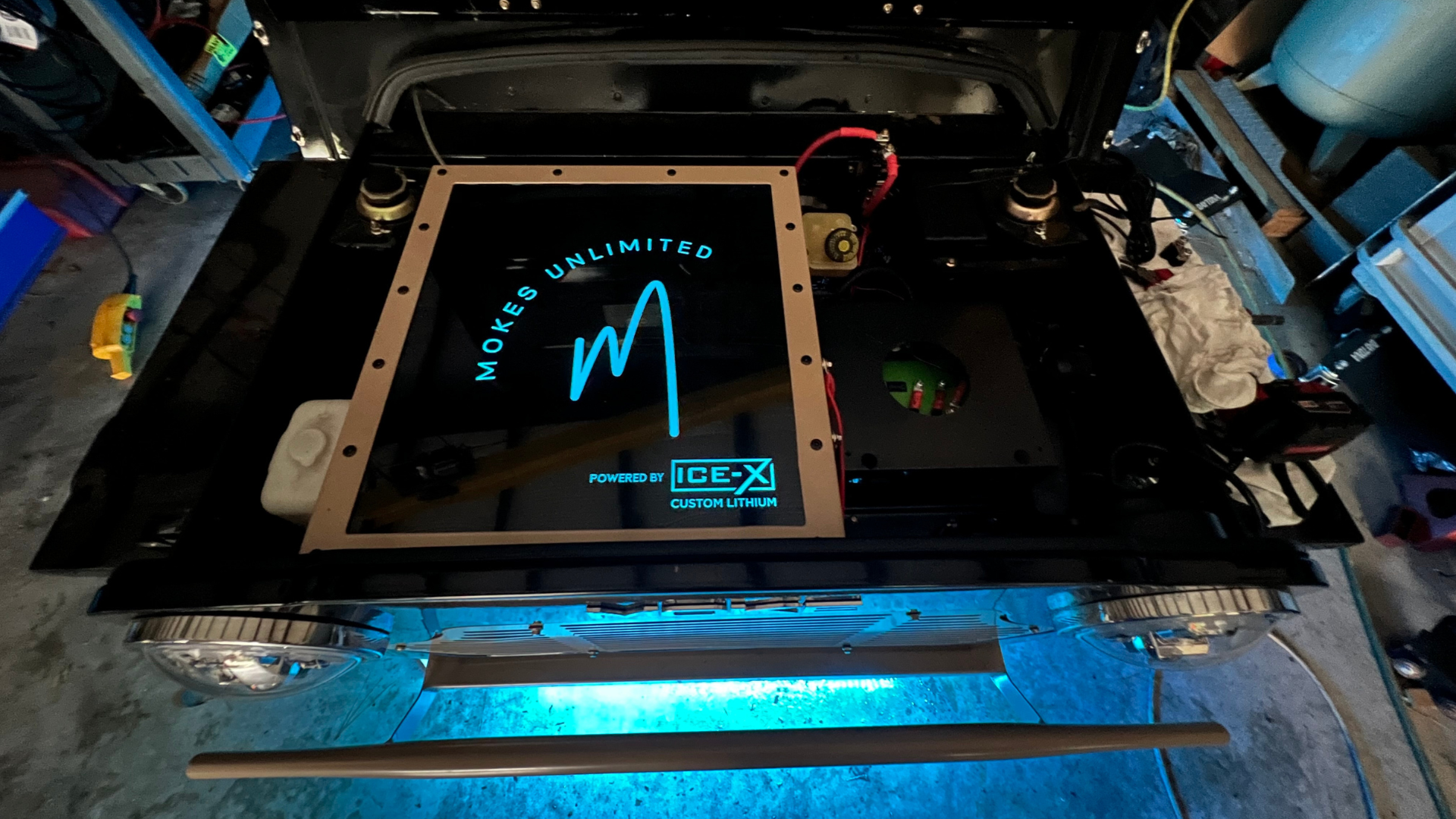 Open car trunk with glowing blue logo, illuminated light bar, and headlights.