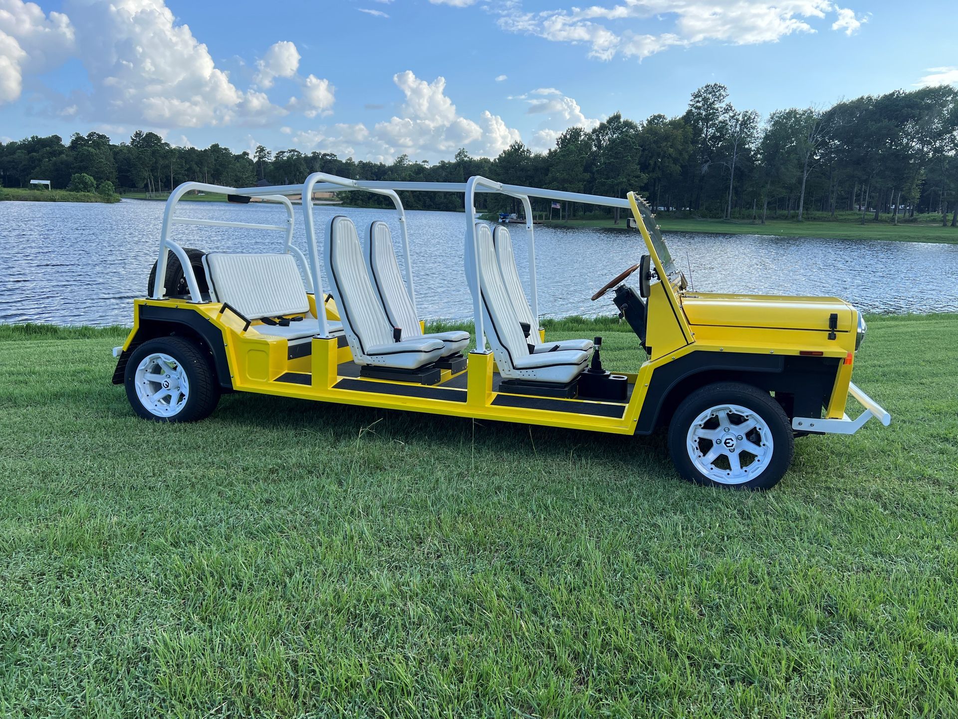 Yellow, open-air vehicle with white seats and roll bars on grass near a lake.