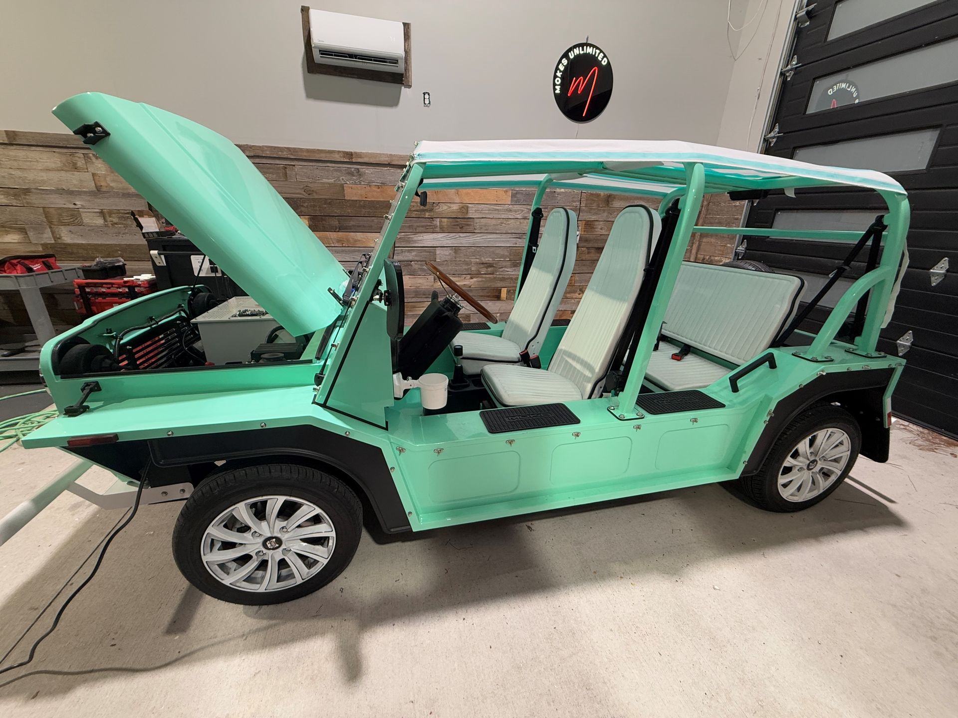 A mint-green, open-air electric vehicle with the hood open, parked indoors.