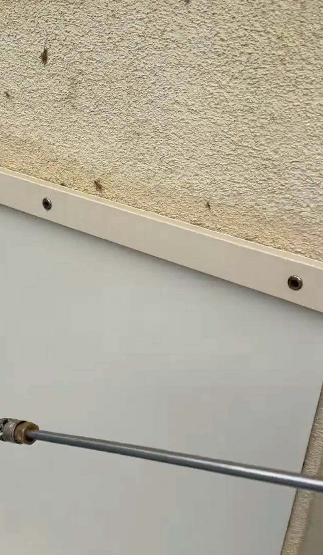 Close-up of a beige wall with a white panel and a metal rod running across the bottom.