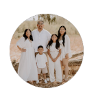 Family of four standing together outdoors in white clothing on a sandy beach