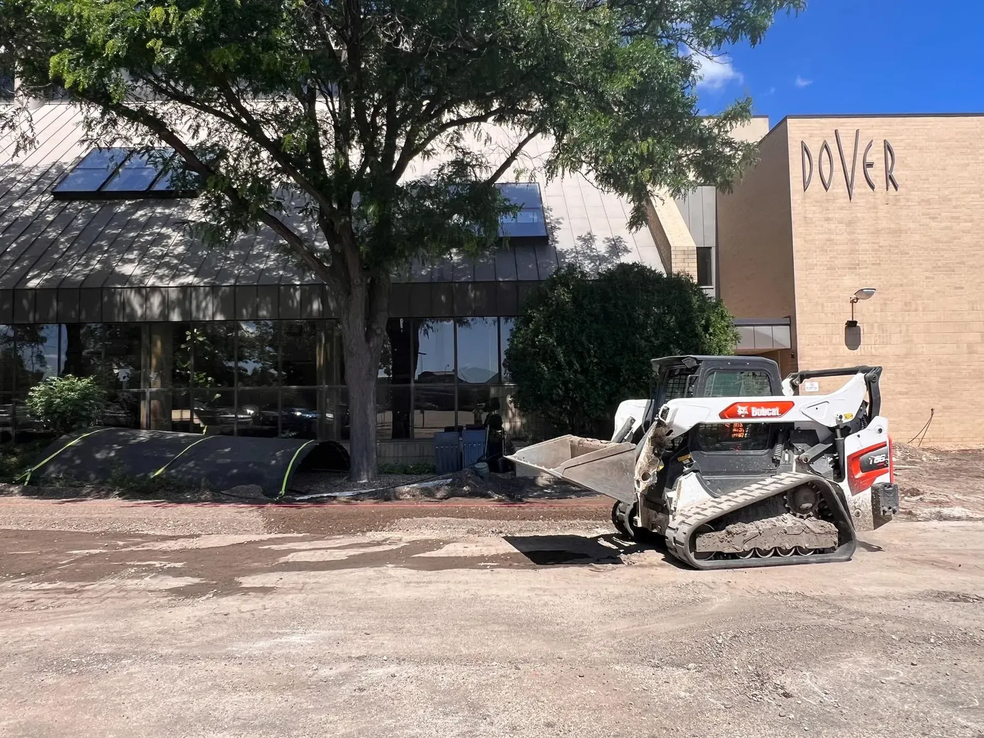 A white Bobcat skid-steer removing debris from a construction site outside a building.