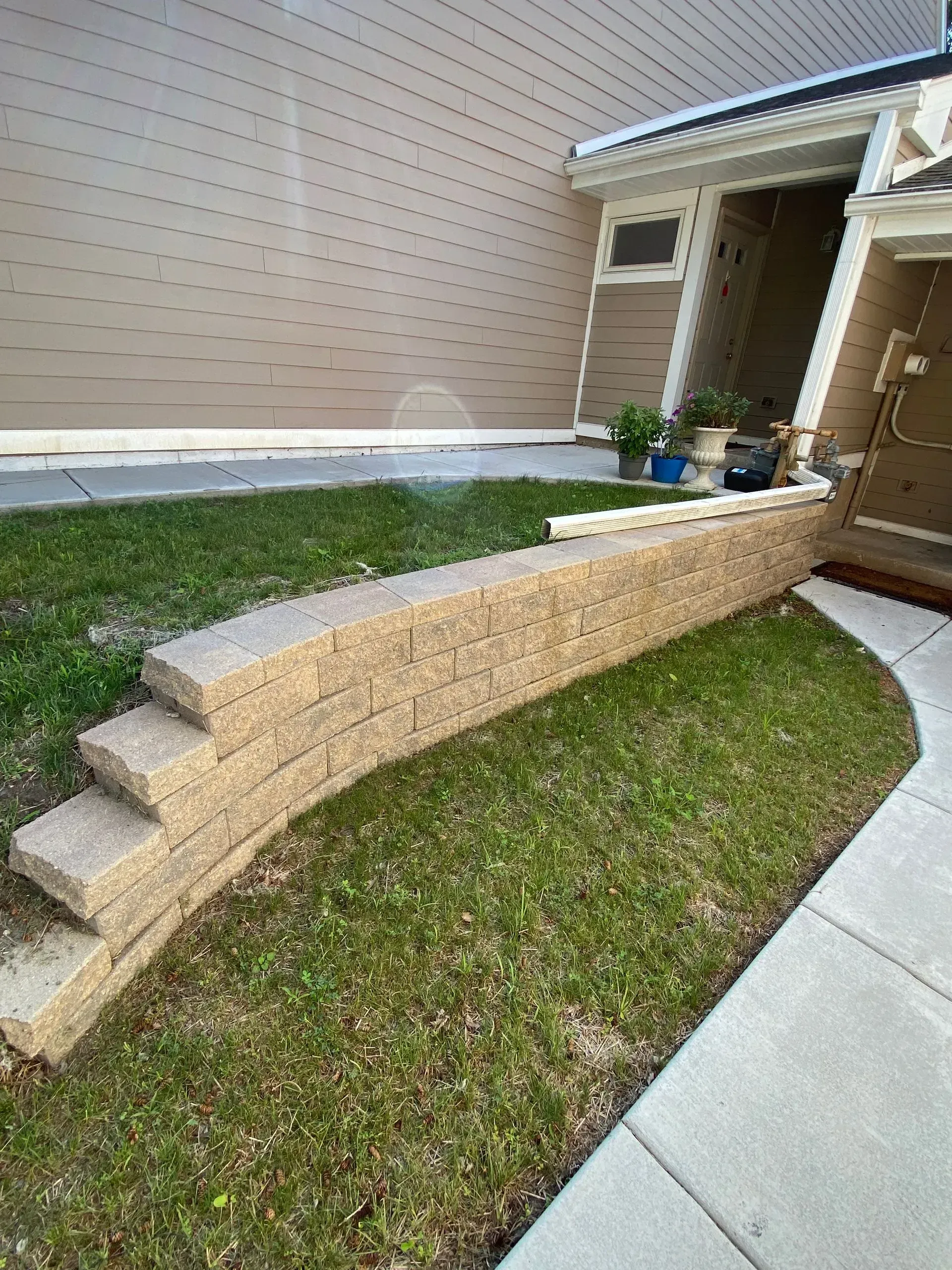 Stone retaining wall with steps in front of a tan garage door and grassy area.