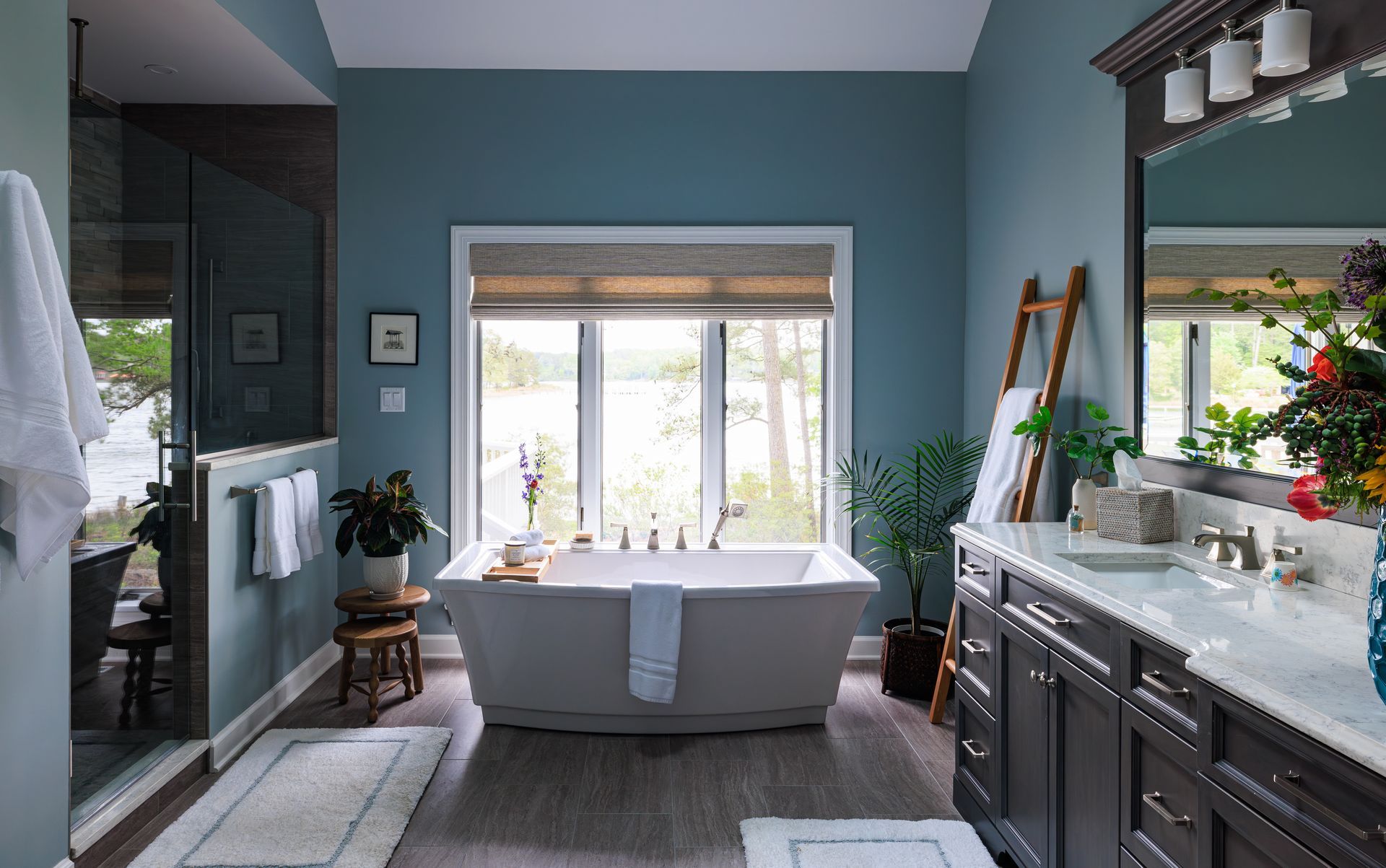 Freestanding soaking tub beside dark wood vanity in blue primary bathroom