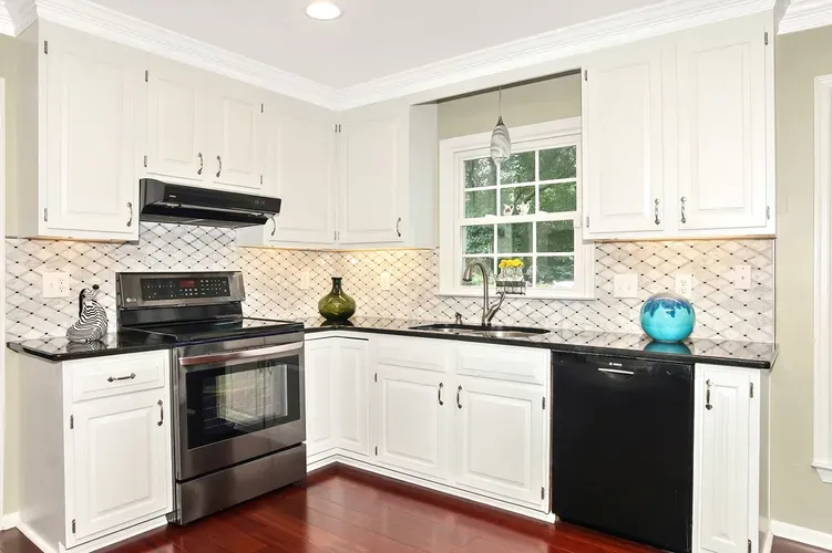 Kitchen with white cabinetry, black appliances, and patterned backsplash