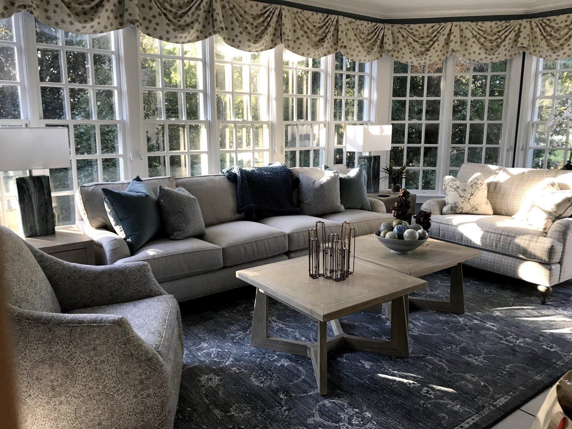 Sunroom seating area with bay windows, layered neutral furniture, and nesting coffee tables