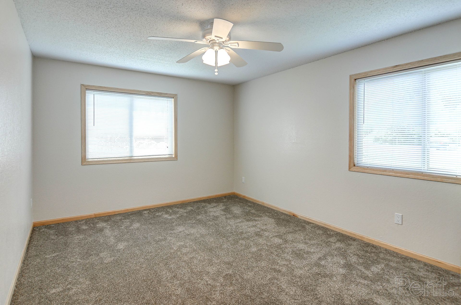 an empty bedroom with a ceiling fan and two windows .