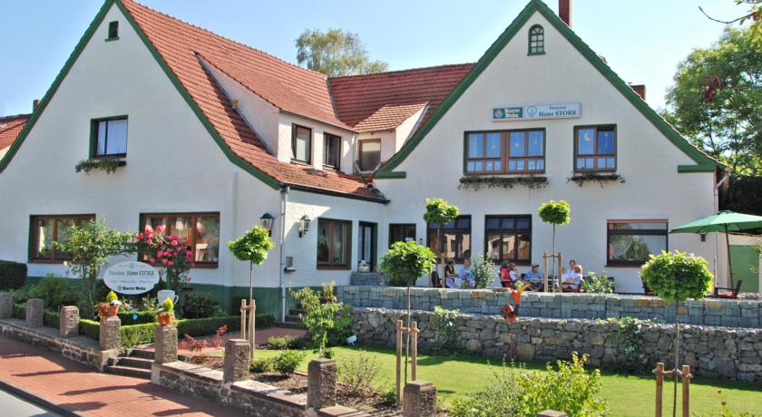 Ein weißes Gebäude mit Giebel und rotem Ziegeldach, das über einen Garten, eine steinerne Stützmauer