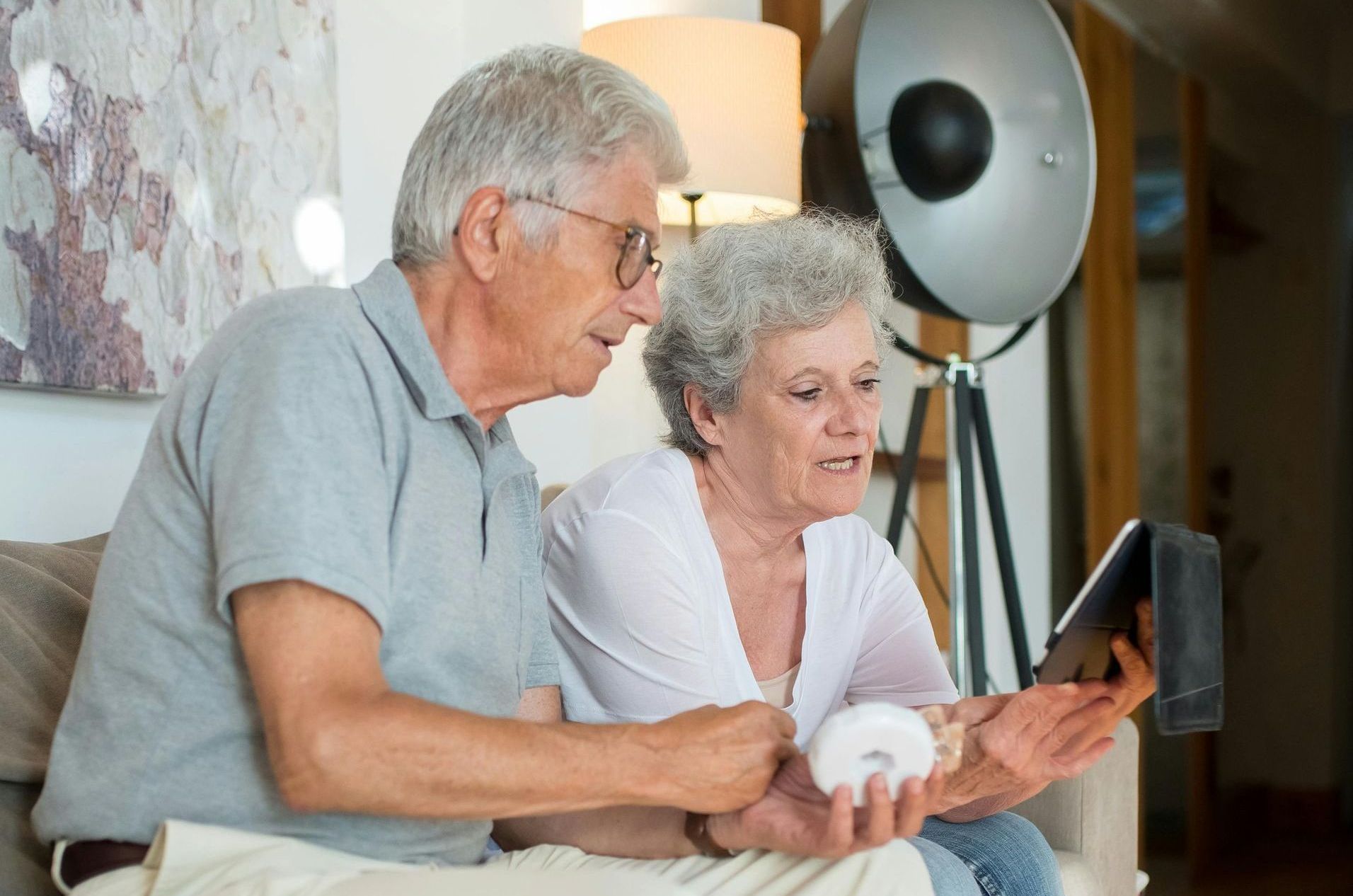 Senior couple looking at tablet together. Woman holds a donut, smiling. Indoors.
