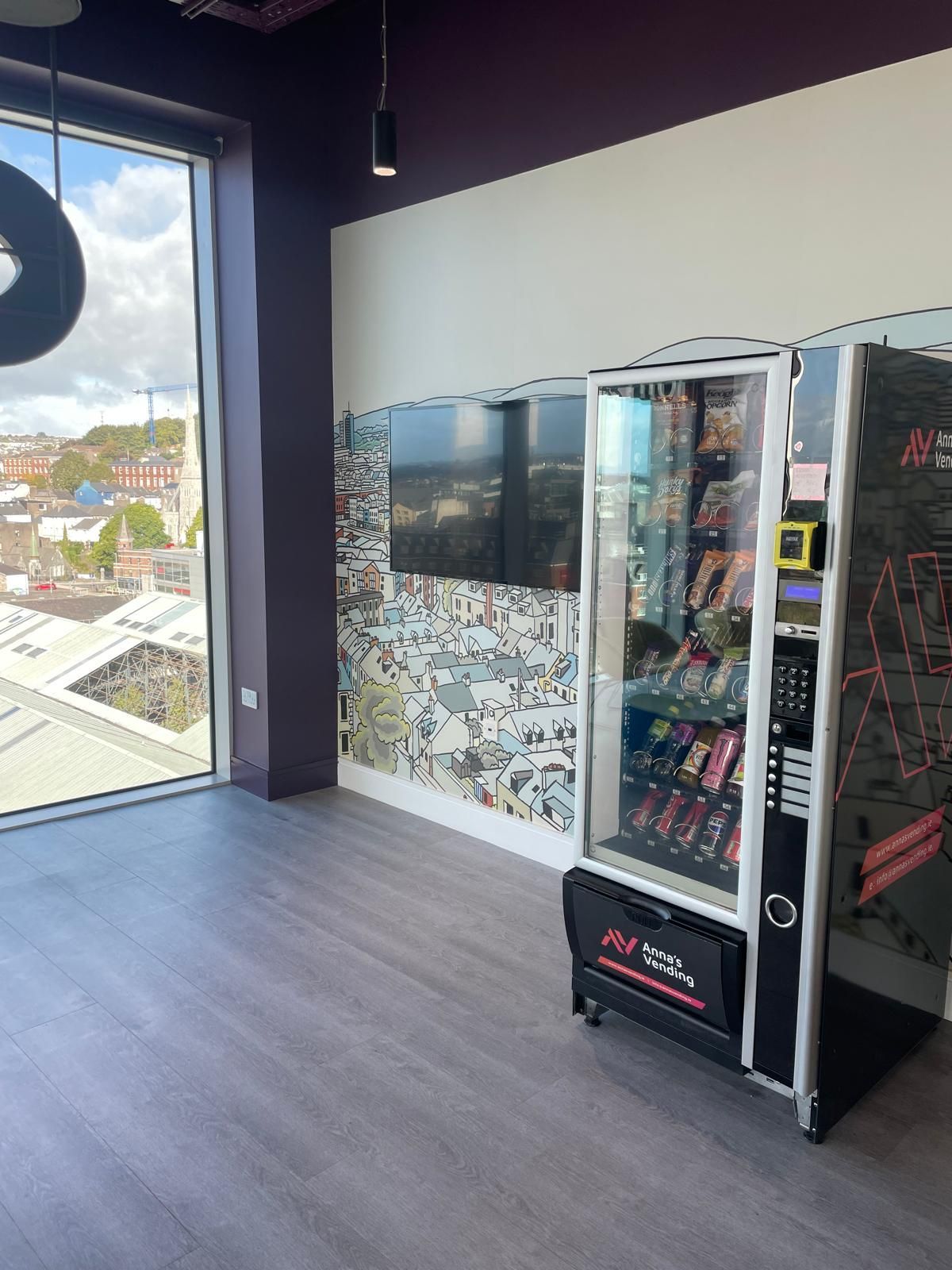 Empty room with vending machines and large window overlooking rooftops