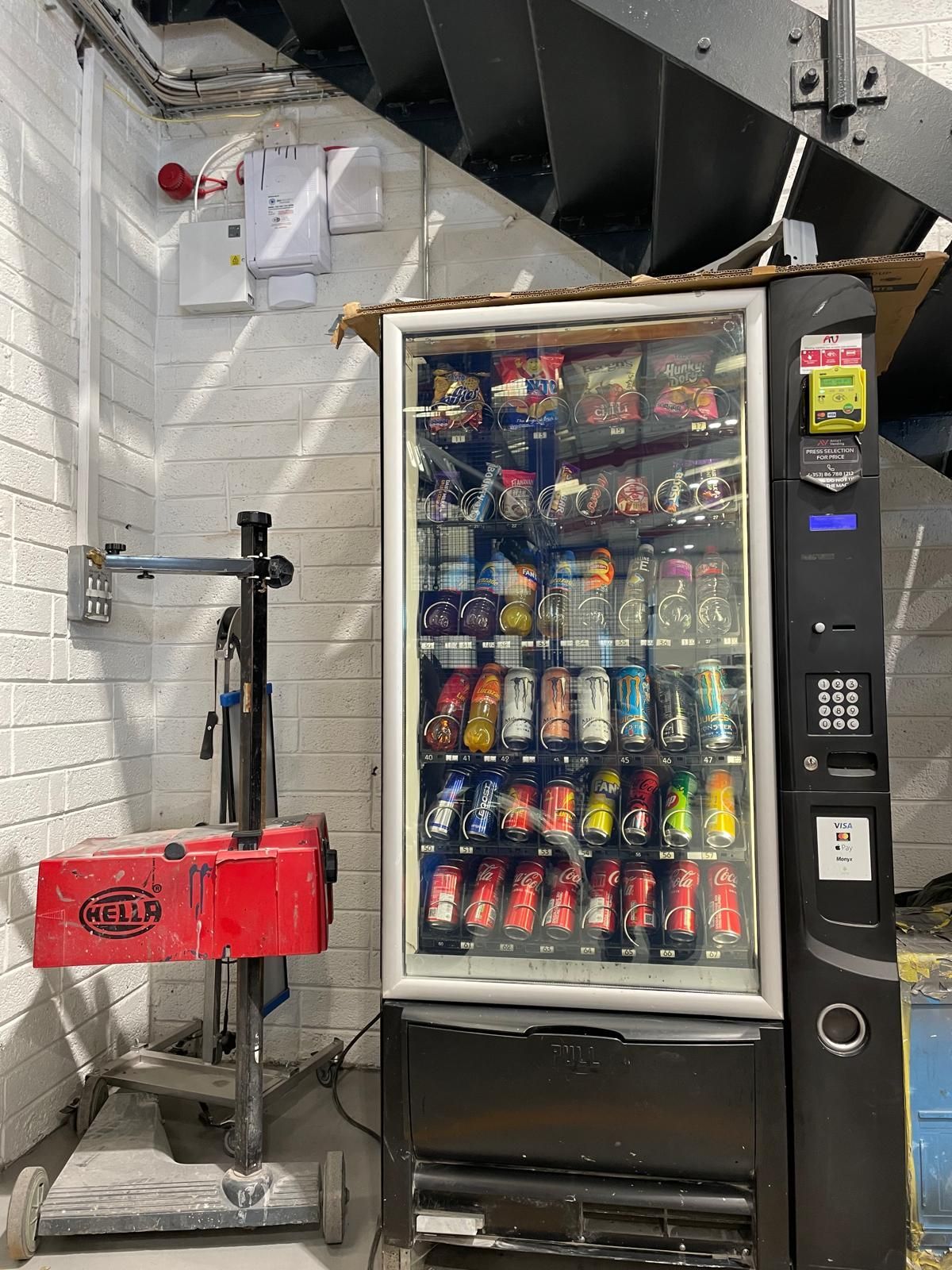 Snack vending machine beside a red cart in an industrial stairwell area
