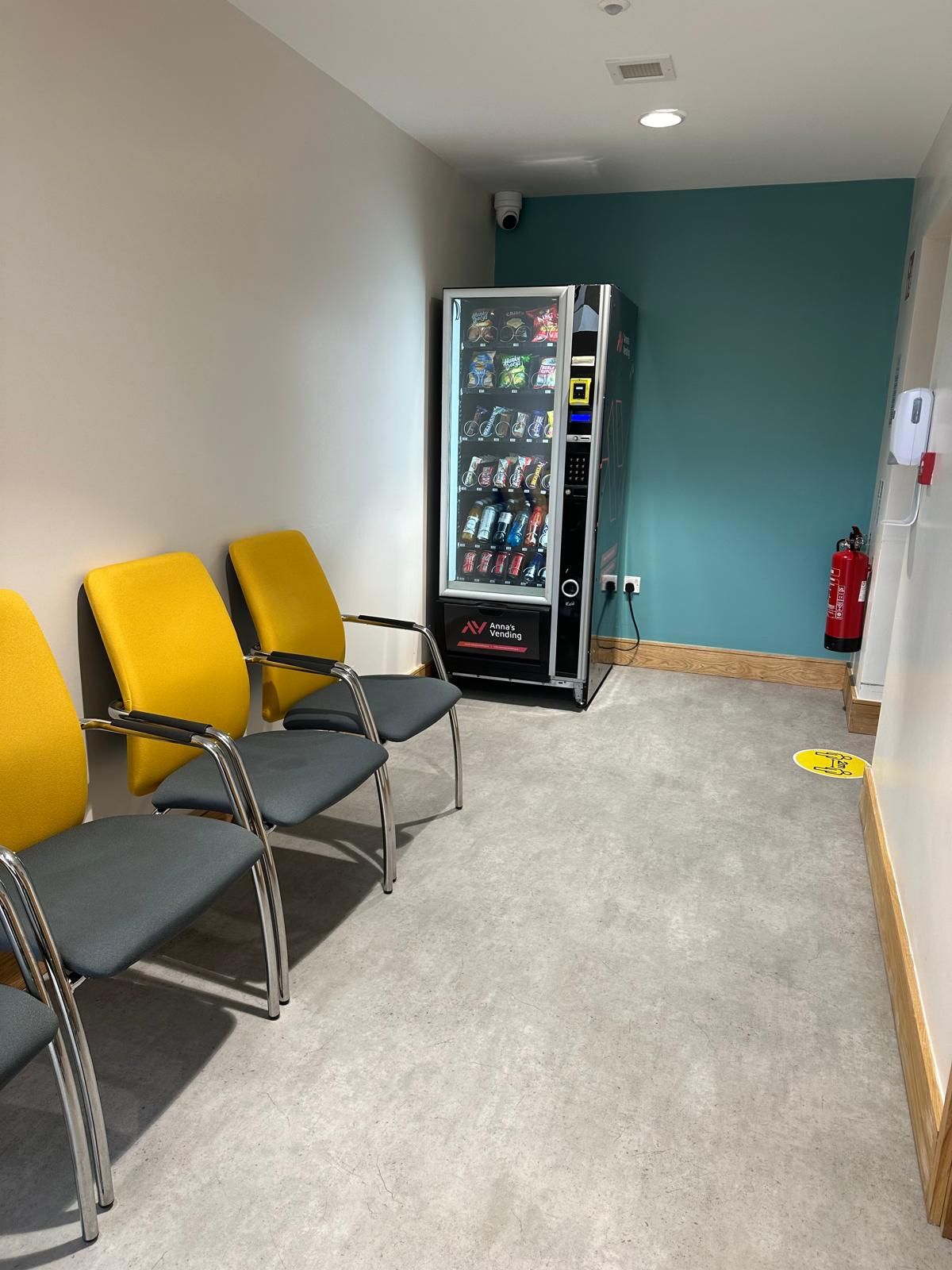 Waiting area with yellow chairs and a vending machine in a hallway