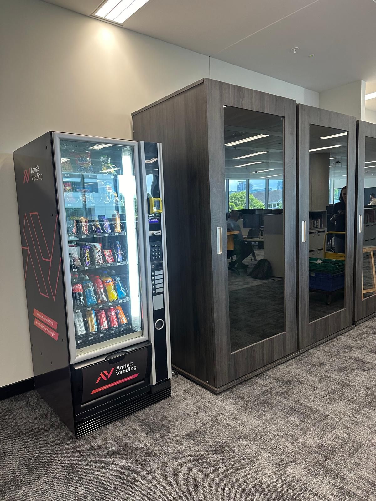 Vending machine beside three dark glass-front phone booths in an office hallway
