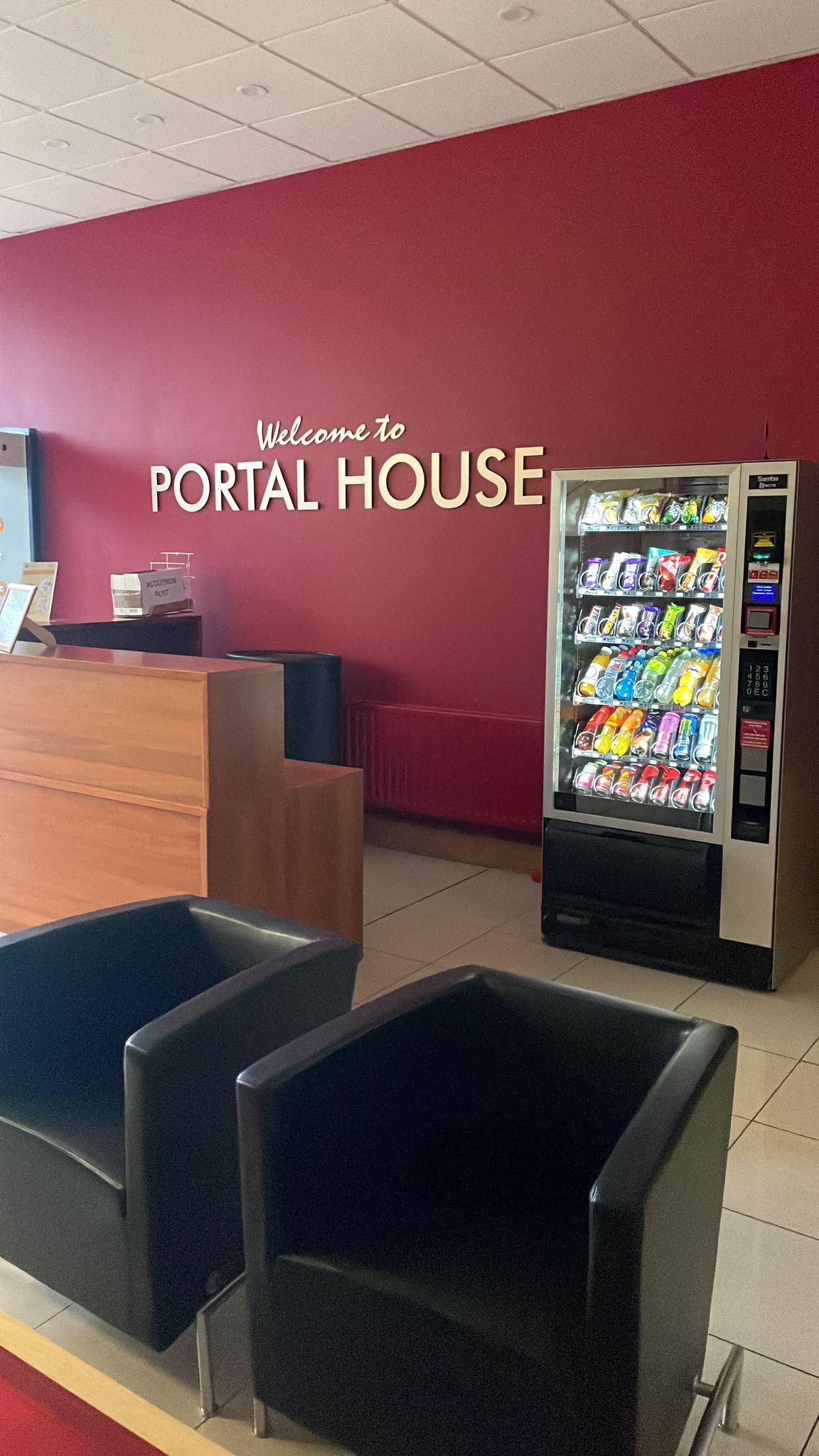 Portal House lobby with reception desk, vending machine, and two black chairs against a maroon wall.