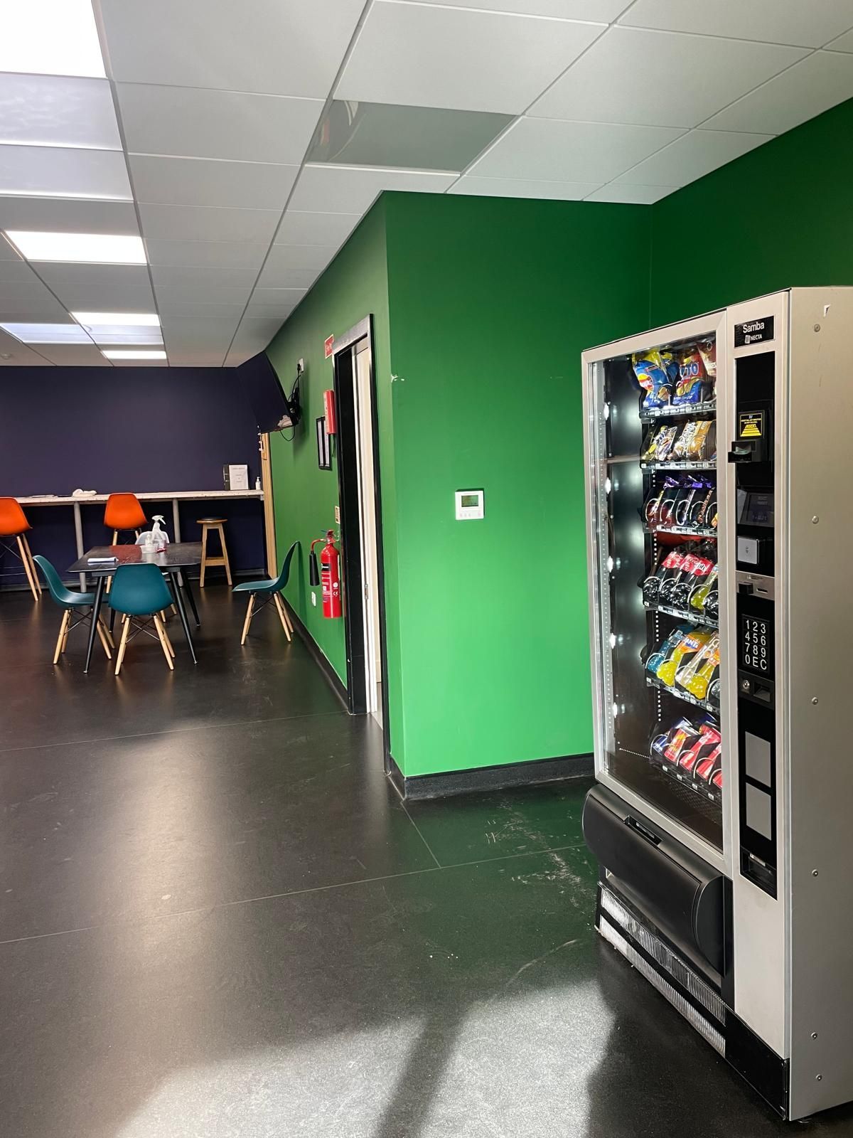 Vending machines along a bright green wall in a lounge with tables and chairs in the background
