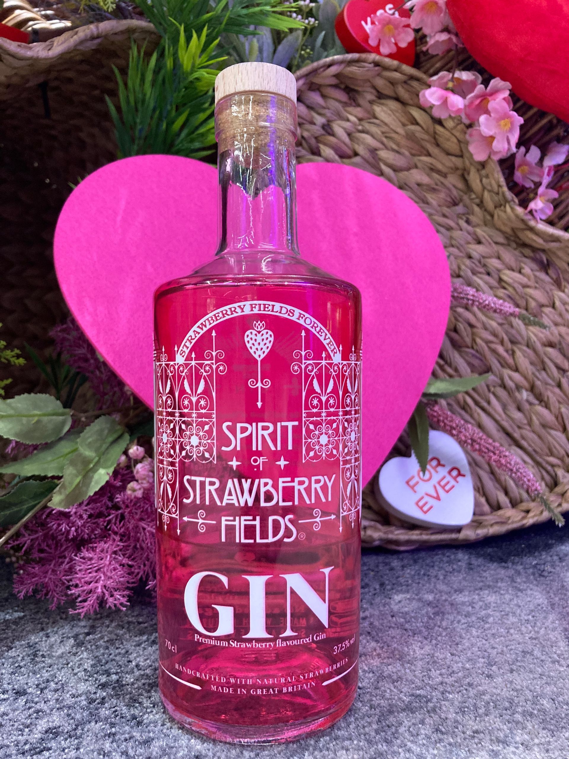 A bottle of strawberry Fields  gin is sitting next to a pink heart which says forever