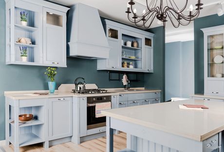 Cucina blu con mobili, fornelli, isola e lampadario decorativo.
