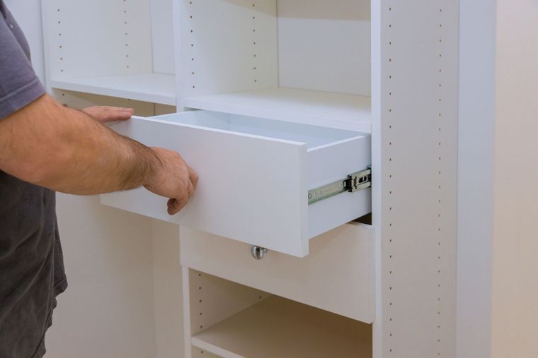 Persona che installa un cassetto bianco in un mobiletto a muro.
