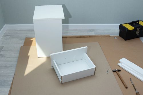 Componenti bianchi del mobile e cassetto disposti per il montaggio, con attrezzi su cartone.