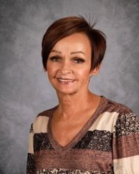 Portrait of a woman smiling against a gray studio backdrop, wearing a patterned V-neck top.