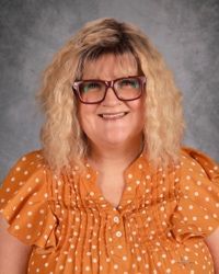 Woman in orange polka-dot blouse and glasses, smiling against a gray studio backdrop.