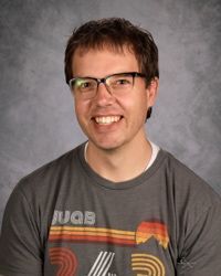 Smiling person with glasses wearing a gray graphic T-shirt against a gray backdrop