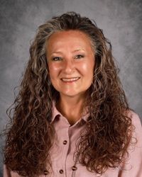 Smiling woman with curly hair in a pink button-up shirt against a gray backdrop